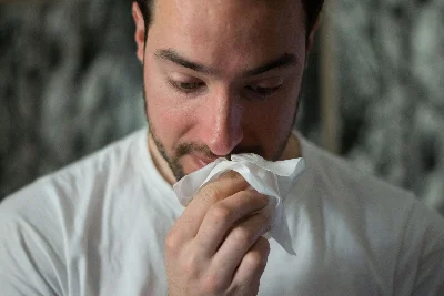 A young white man blowing his nose with a tissue